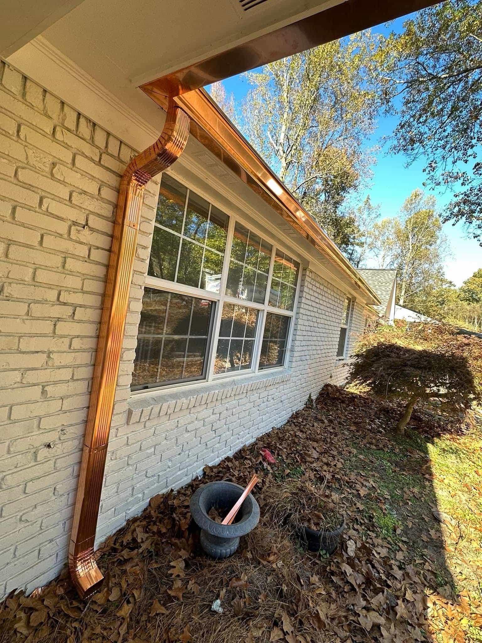 Copper downspout installed on white brick wall with collector box detail