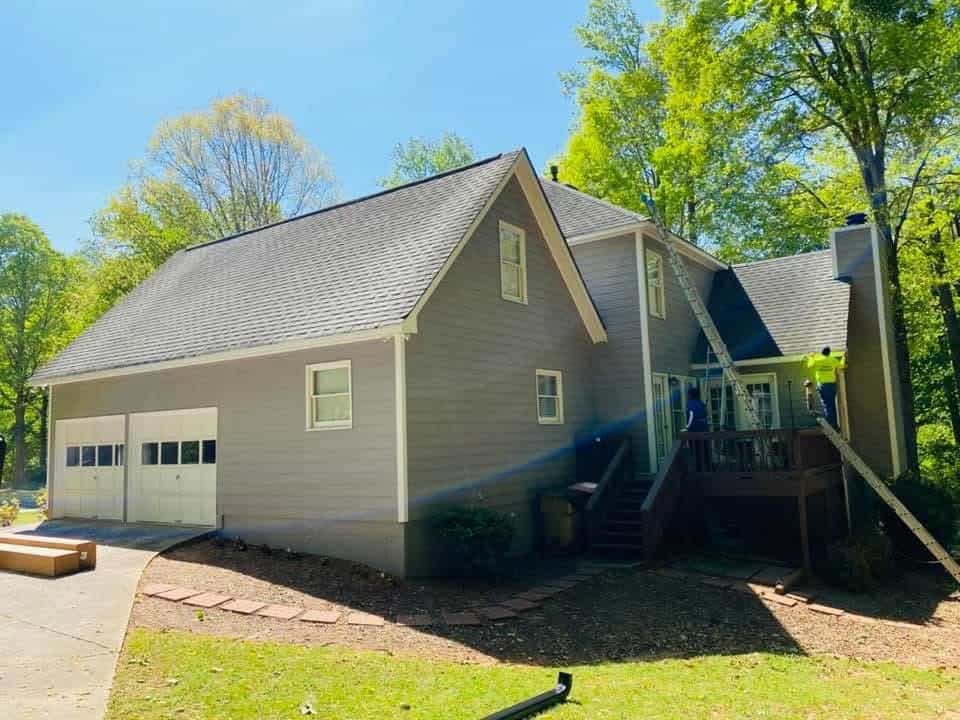Crew members actively installing gutters with ladders on craftsman home